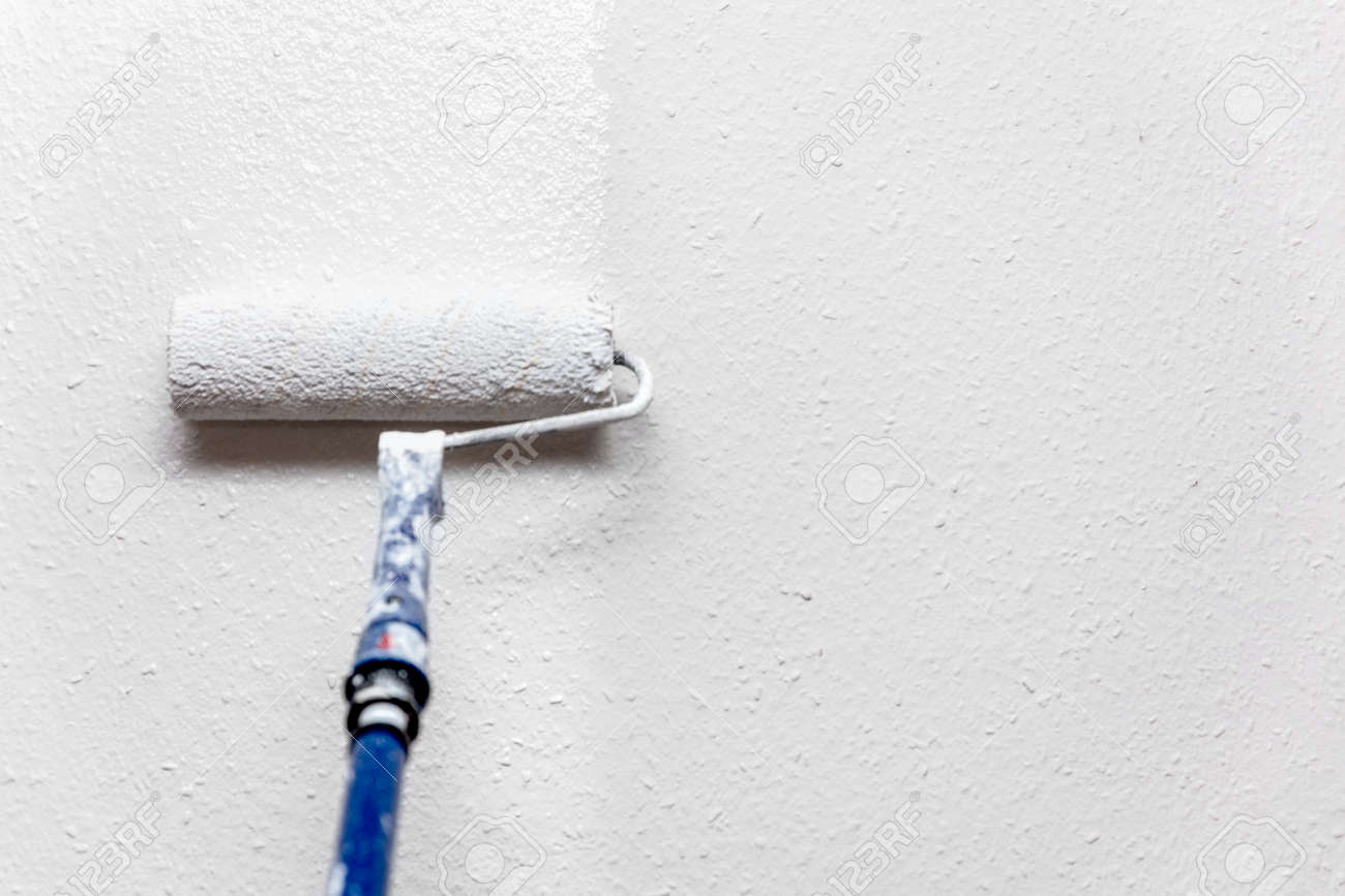 156277318-a-painter-paints-a-wall-fresh-with-white-paint-and-paint-roller